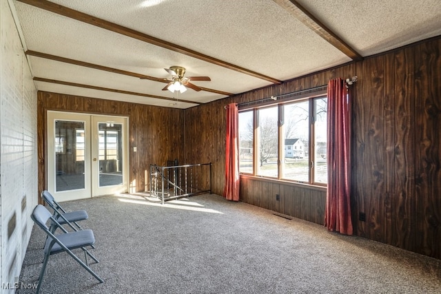 interior space featuring beamed ceiling, a textured ceiling, french doors, carpet, and wooden walls