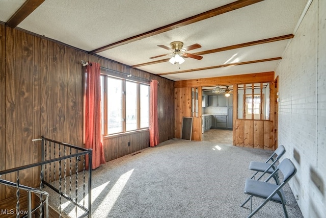 interior space featuring beam ceiling, carpet flooring, wood walls, and a textured ceiling