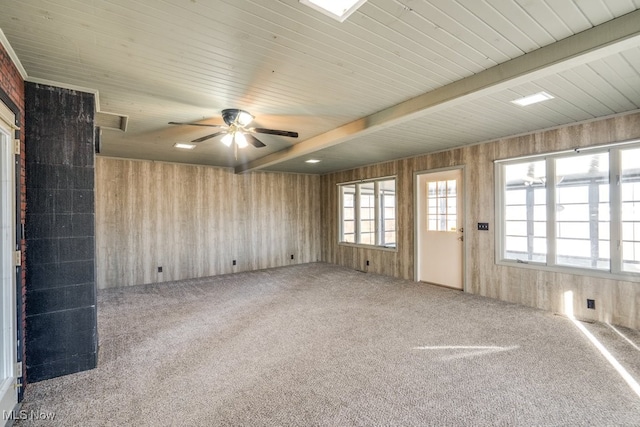 unfurnished room with beam ceiling, wooden walls, a healthy amount of sunlight, and carpet