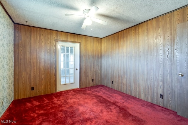 carpeted spare room with a ceiling fan, wood walls, and a textured ceiling