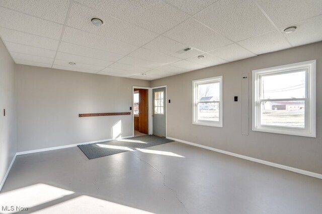 empty room with finished concrete flooring, baseboards, and a drop ceiling
