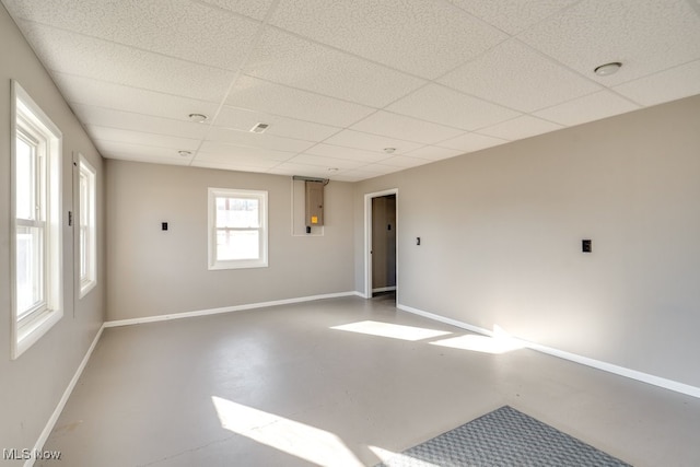 spare room with finished concrete flooring, baseboards, and a paneled ceiling