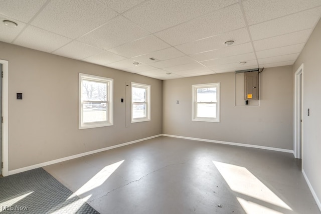 unfurnished room featuring electric panel, a drop ceiling, baseboards, and concrete flooring