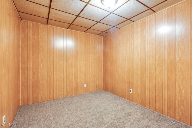 carpeted empty room featuring wooden walls and a drop ceiling