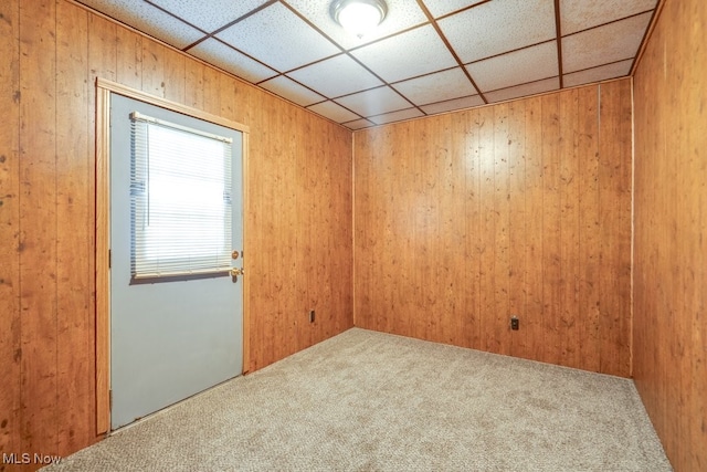 empty room featuring a drop ceiling, wood walls, and carpet floors
