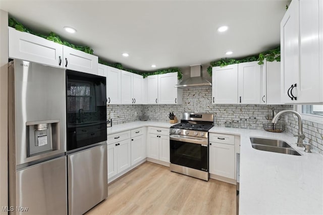 kitchen with light wood-type flooring, a sink, stainless steel appliances, wall chimney exhaust hood, and tasteful backsplash