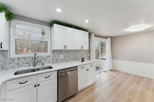 kitchen with light countertops, decorative backsplash, stainless steel dishwasher, light wood-style floors, and a sink