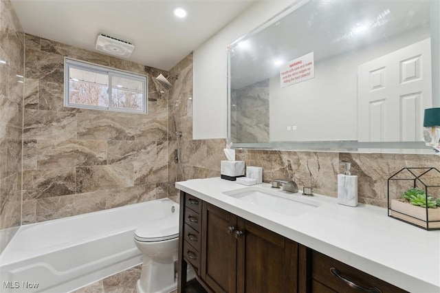 full bathroom featuring toilet, backsplash, vanity, tile walls, and shower / bathtub combination