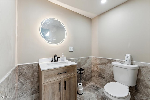 bathroom with a wainscoted wall, toilet, tile walls, and vanity