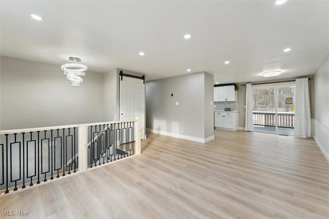 unfurnished room with a barn door, recessed lighting, light wood-type flooring, and baseboards