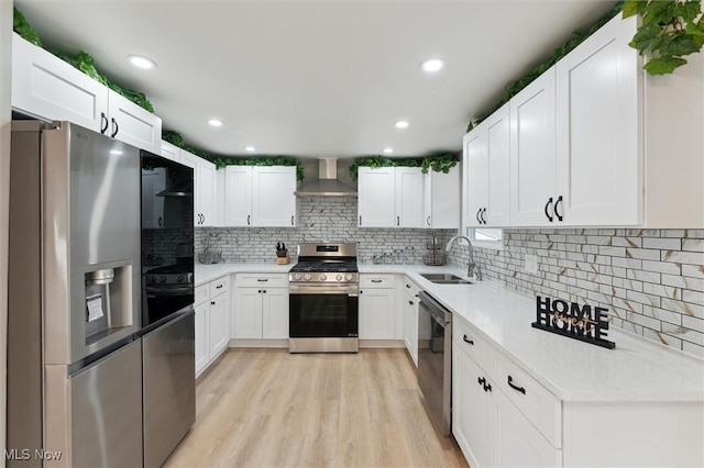 kitchen with light wood-type flooring, a sink, white cabinetry, stainless steel appliances, and wall chimney range hood