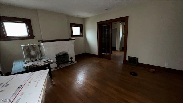 unfurnished living room featuring visible vents, baseboards, a brick fireplace, and wood finished floors