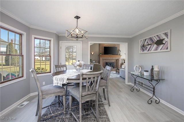 dining room with visible vents, ornamental molding, light wood-style floors, baseboards, and a brick fireplace