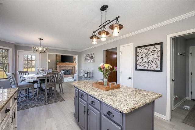 kitchen featuring light wood-style floors, a fireplace, crown molding, light stone countertops, and hanging light fixtures