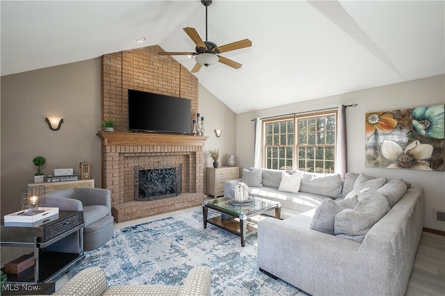 living area featuring ceiling fan, a brick fireplace, wood finished floors, and vaulted ceiling