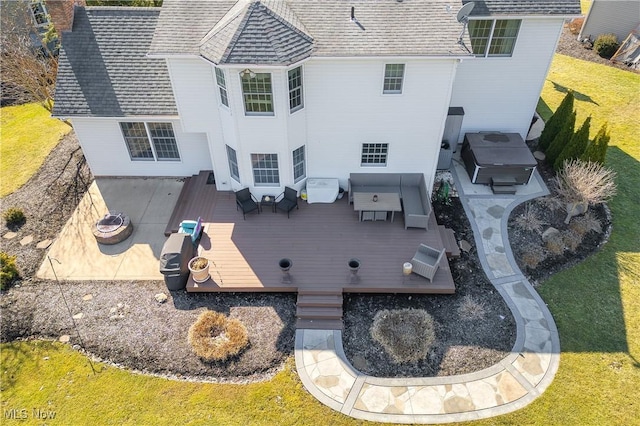 back of property with a lawn, roof with shingles, a deck, and a hot tub