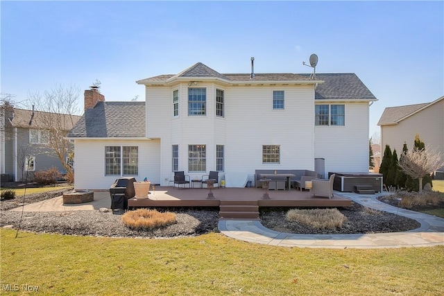 rear view of property featuring a yard, a chimney, an outdoor living space with a fire pit, a hot tub, and a deck