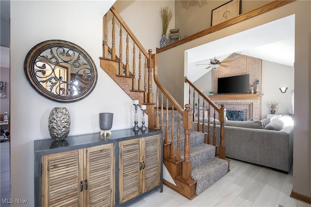 staircase with vaulted ceiling, a fireplace, ceiling fan, and wood finished floors