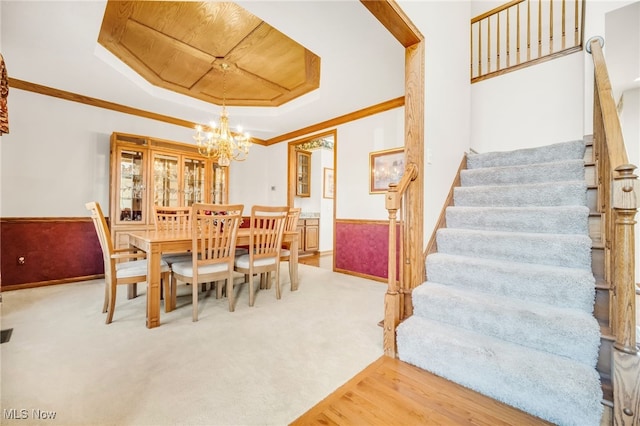 dining area featuring a tray ceiling, stairway, crown molding, and wainscoting