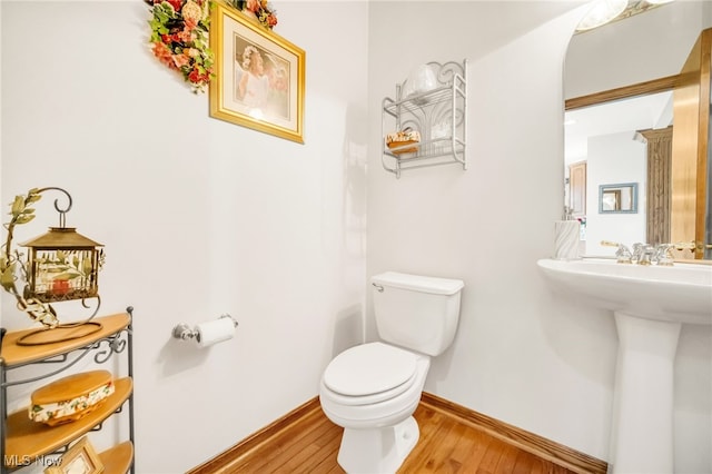 half bath with toilet, wood finished floors, baseboards, and a sink