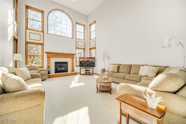 living room with plenty of natural light, carpet, a towering ceiling, and a glass covered fireplace