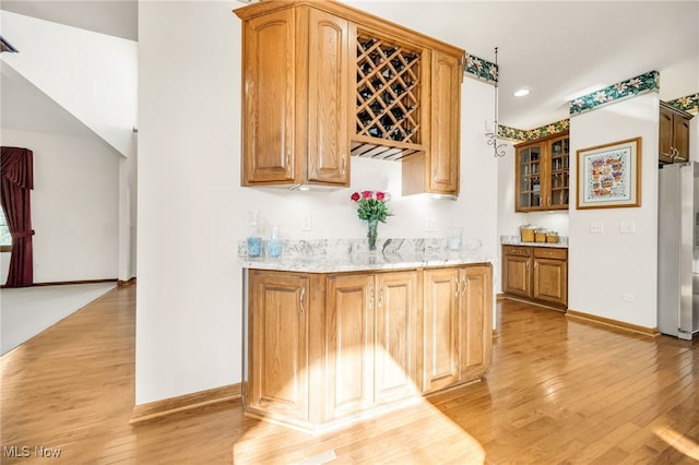 bar with light wood-type flooring, baseboards, wet bar, and freestanding refrigerator