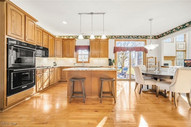 kitchen featuring a center island, light wood-type flooring, decorative backsplash, hanging light fixtures, and black appliances