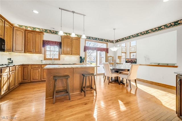 kitchen featuring a kitchen island, decorative backsplash, black microwave, decorative light fixtures, and light wood-type flooring