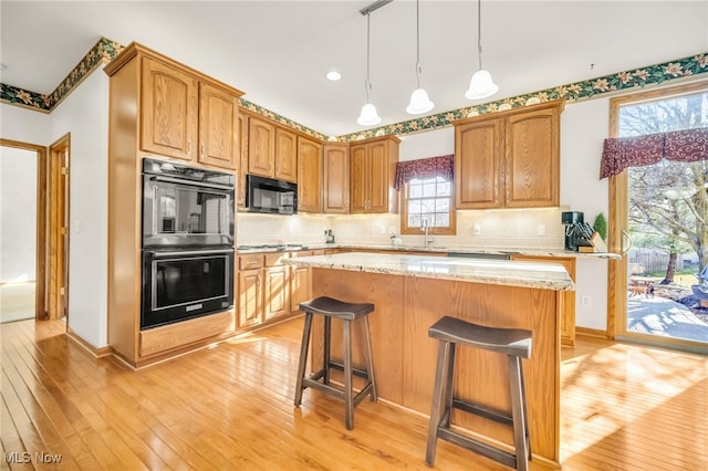 kitchen featuring a breakfast bar area, decorative backsplash, light wood-style flooring, black appliances, and a sink