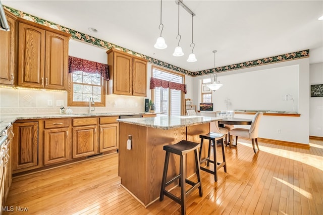 kitchen with light wood-style flooring, a sink, a kitchen island, tasteful backsplash, and light stone countertops