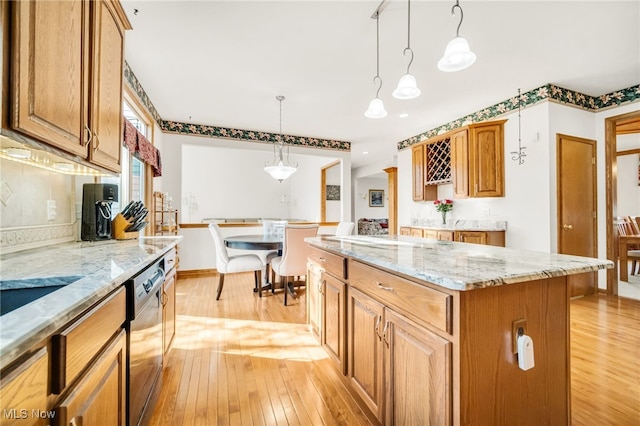 kitchen with light stone counters, light wood-style floors, and stainless steel dishwasher