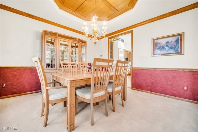 dining space featuring crown molding, light colored carpet, wainscoting, an inviting chandelier, and a raised ceiling