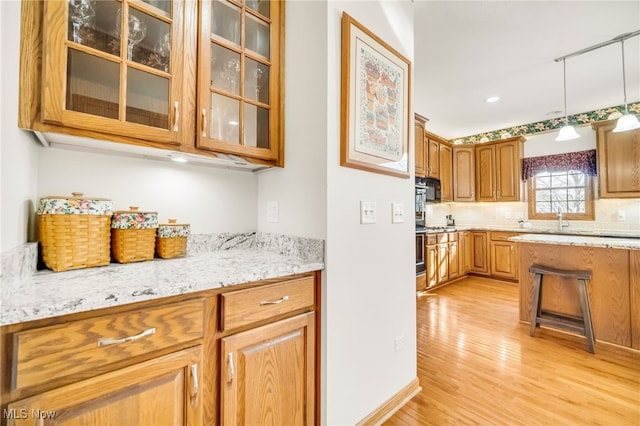 kitchen with brown cabinetry, decorative light fixtures, glass insert cabinets, and light wood-style floors