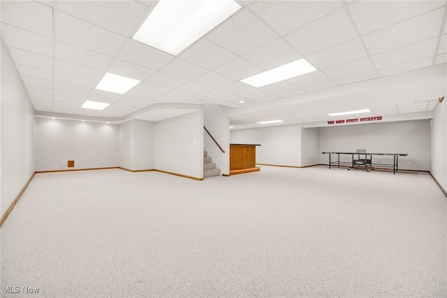 finished basement featuring a paneled ceiling, carpet, stairs, and baseboards