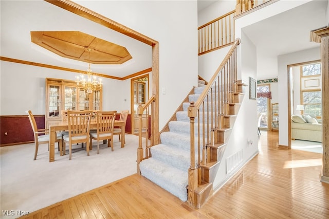 stairs with a tray ceiling, visible vents, hardwood / wood-style floors, and crown molding