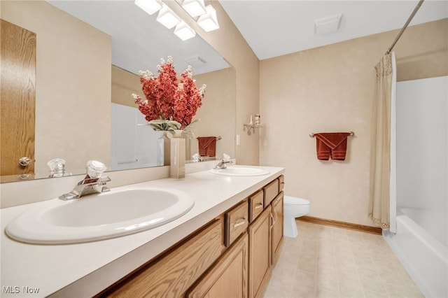 bathroom with double vanity, toilet, baseboards, and a sink