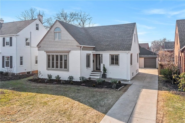 view of front of house featuring an outbuilding, a front yard, a shingled roof, a detached garage, and brick siding