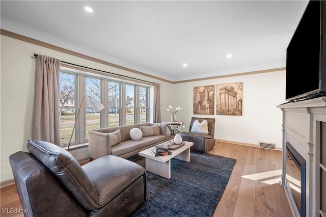 living room with visible vents, crown molding, a fireplace with flush hearth, recessed lighting, and wood finished floors