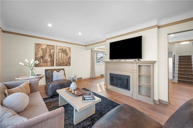 living room featuring stairway, ornamental molding, a glass covered fireplace, and wood finished floors