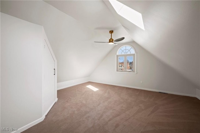 additional living space with baseboards, vaulted ceiling with skylight, carpet floors, and a ceiling fan