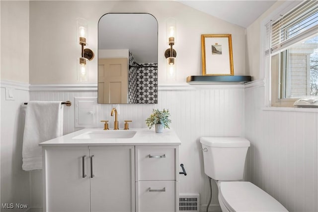 full bath with vanity, lofted ceiling, toilet, and wainscoting