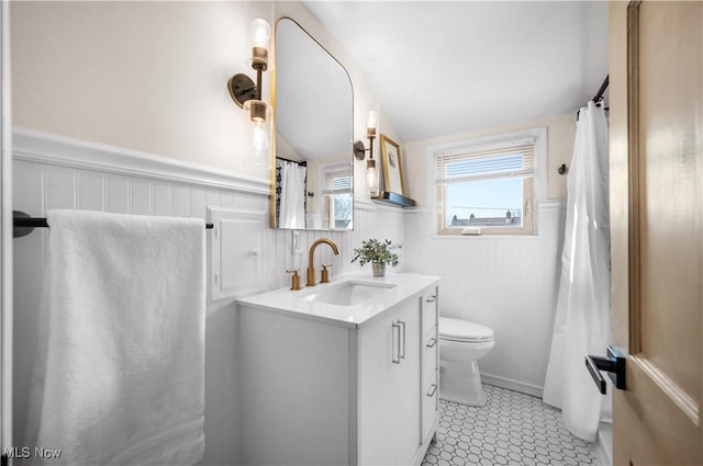 full bathroom with a wainscoted wall, toilet, a shower with shower curtain, vanity, and vaulted ceiling