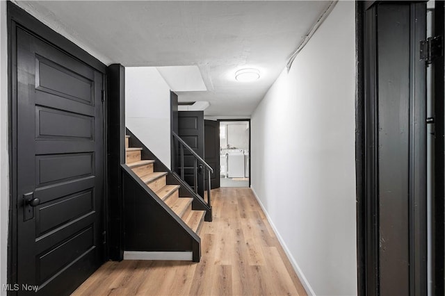 corridor featuring light wood-type flooring, baseboards, and stairs