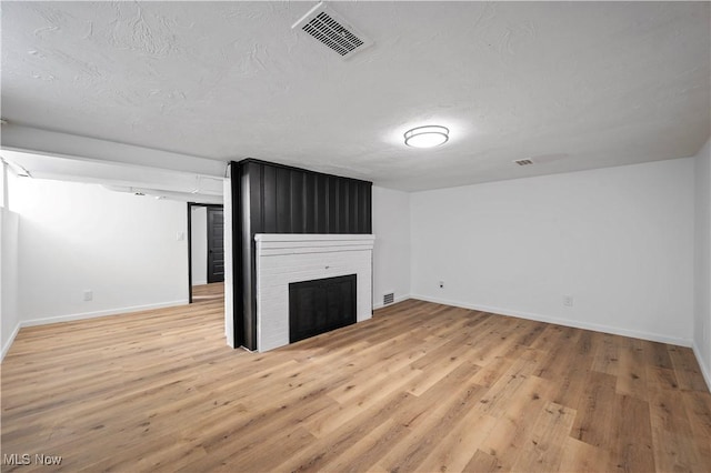 unfurnished living room featuring visible vents, a textured ceiling, a large fireplace, light wood-style floors, and baseboards