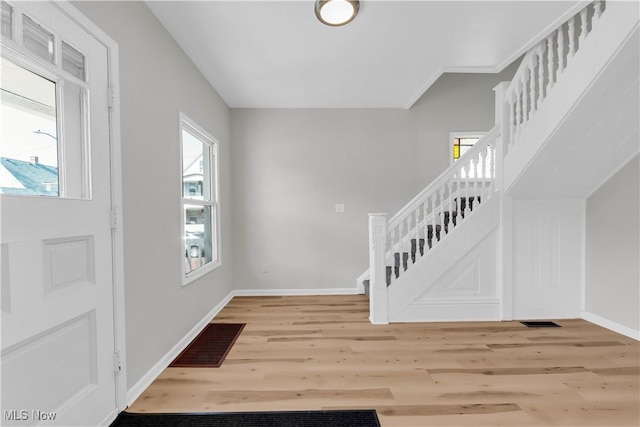 foyer entrance featuring visible vents, baseboards, wood finished floors, and stairway