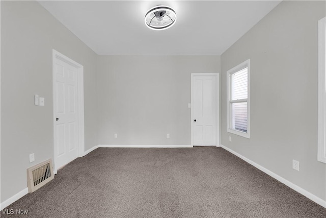 unfurnished room with dark colored carpet, visible vents, and baseboards