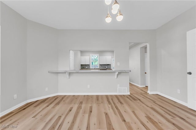 unfurnished living room featuring light wood-style flooring, baseboards, visible vents, and a chandelier