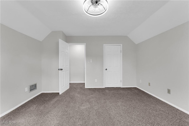 interior space featuring visible vents, dark carpet, baseboards, and vaulted ceiling