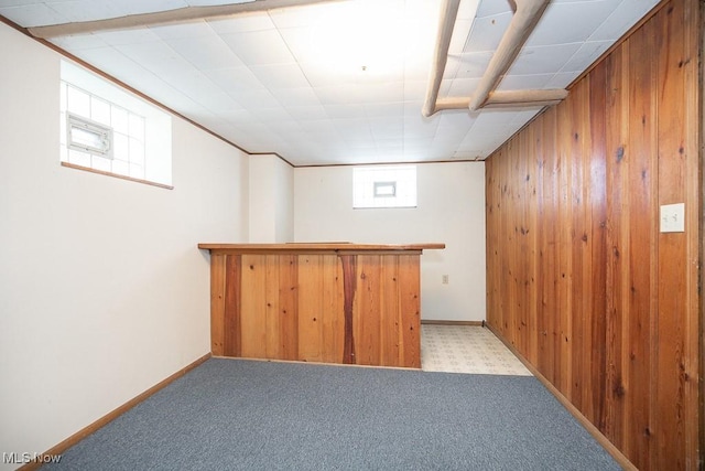 basement with wooden walls, baseboards, a dry bar, and light carpet