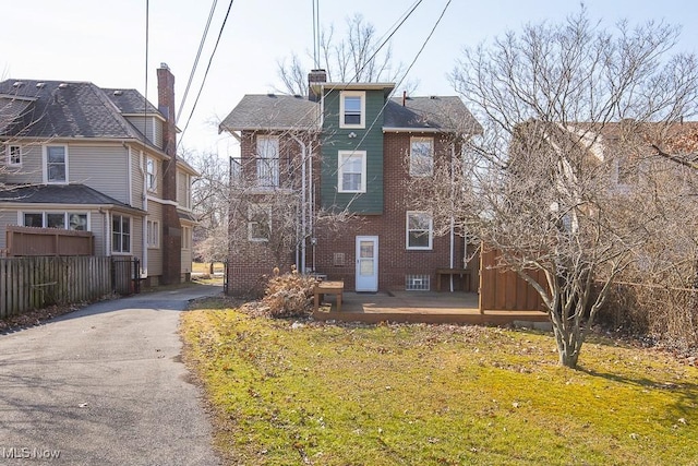 rear view of house featuring brick siding, a lawn, driveway, and fence